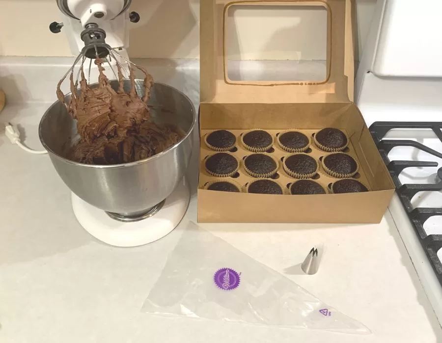 Stand mixer with freshly made chocolate icing next to a bakery box of chocolate cupcakes made with freshly milled flour.