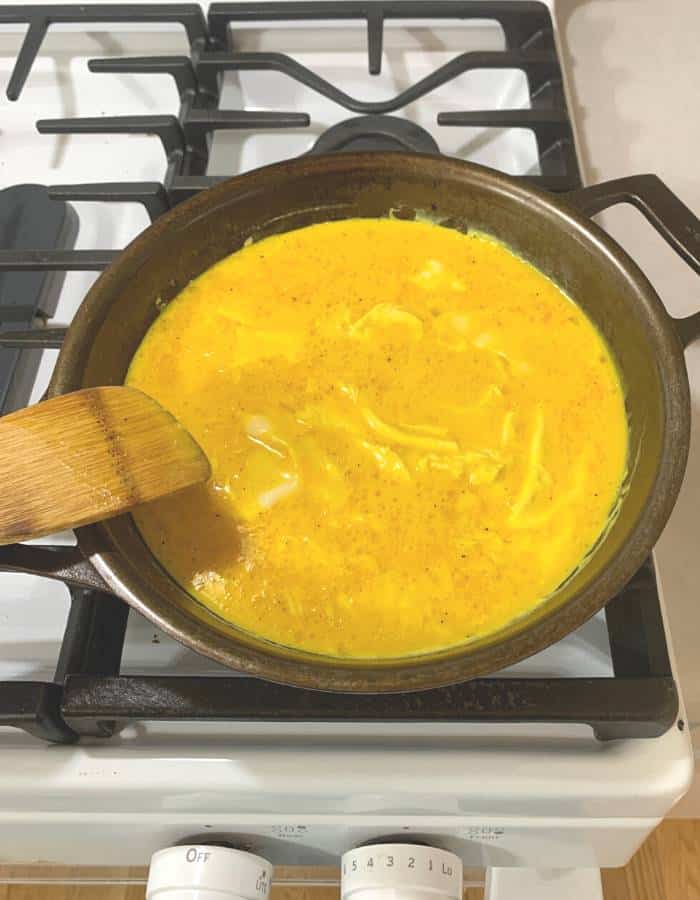 Scrambled eggs cooking in a cast iron skillet on a stove.