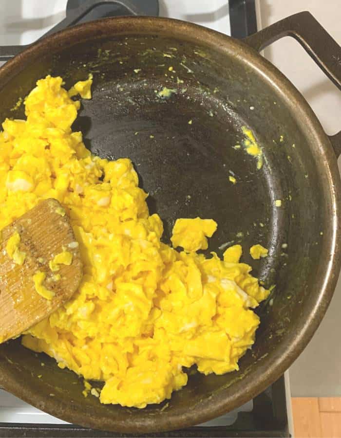 Scrambled eggs in a cast iron skillet with a wooden spoon.