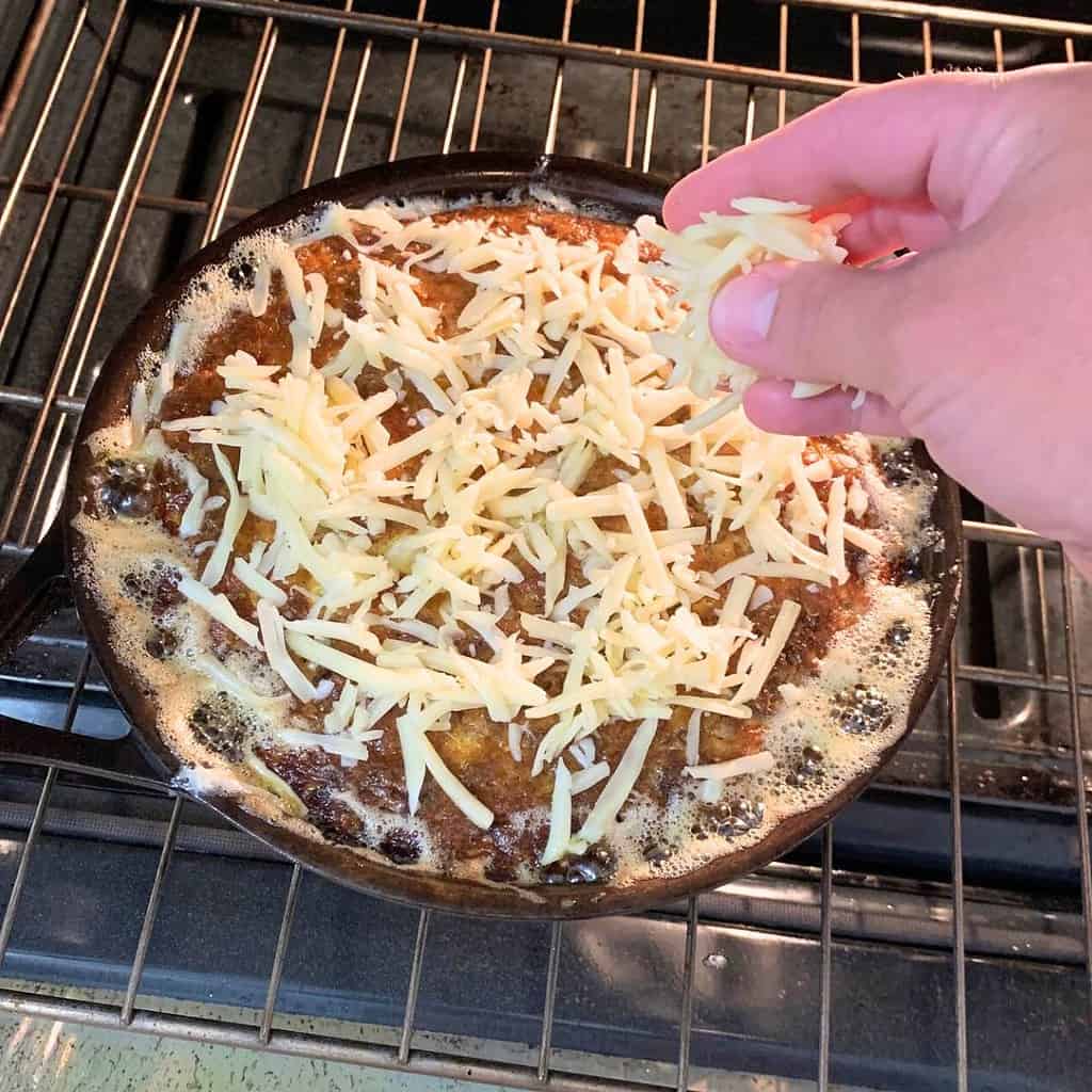 Woman sprinkling white cheddar cheese on top of a hot chicken liver souffle in the oven.