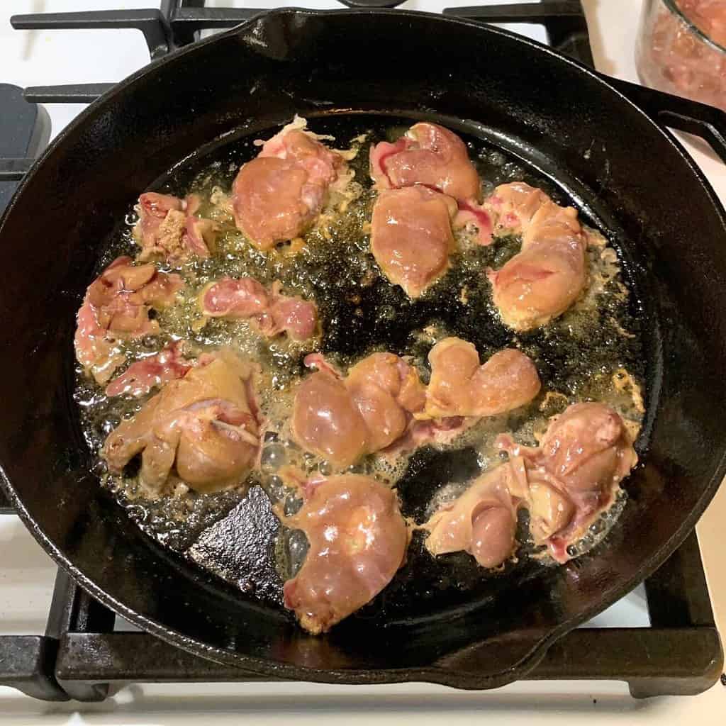 Chicken livers cooking in a cast iron skillet on the stove.