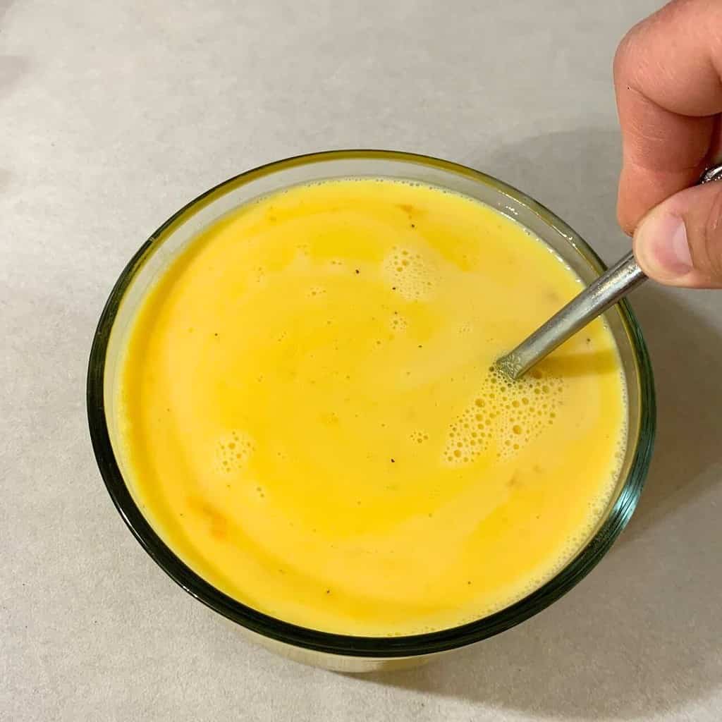 Woman mixing eggs and milk in a glass bowl.