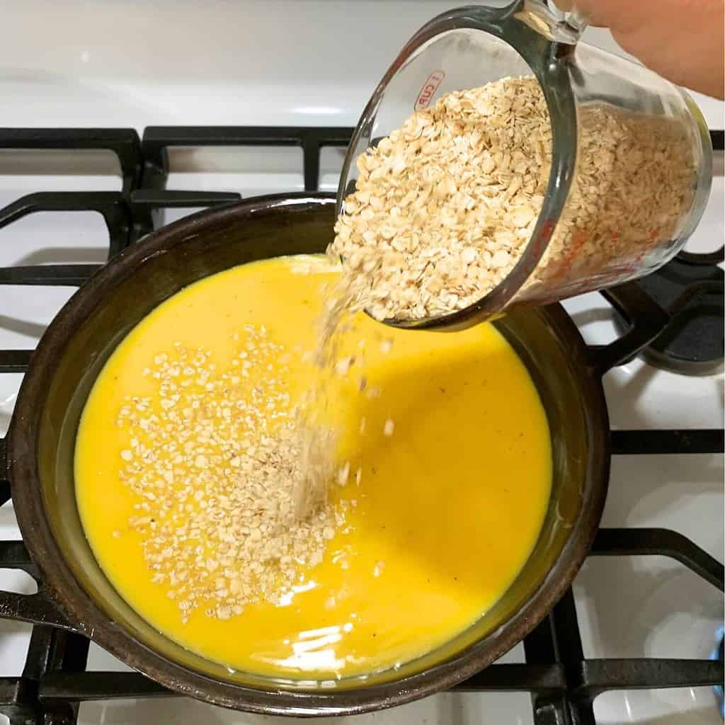 Woman pouring oats into an egg mixture in a cast iron skillet on the stove.