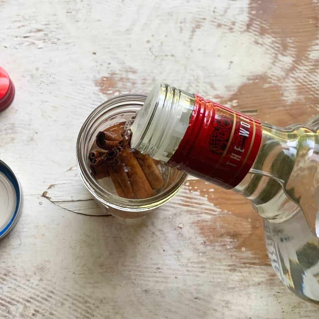 Cassia vs ceylon cinnamon.  A woman filling a glass jar with cinnamon sticks up with vodka.