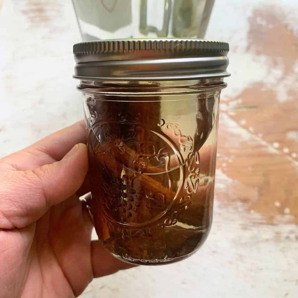 Cassia vs ceylon cinnamon. Woman holding a glass mason jar with cinnamon sticks submerged under vodka.