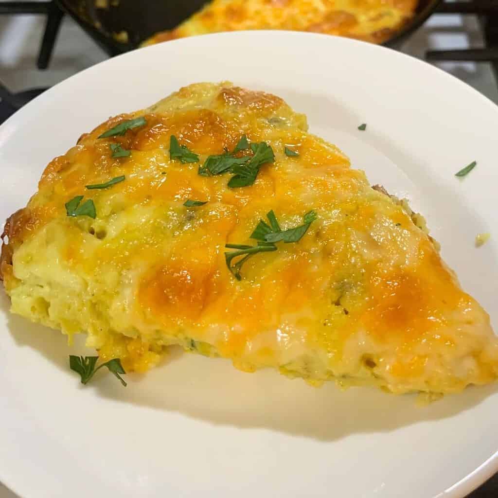 Woman holding a white plate with cheesy zucchini casserole that's fresh from the oven. A sprinkle of fresh parsley is on top.