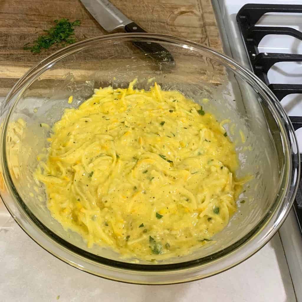 Cheesy zucchini casserole ingredients combined in a glass bowl on a kitchen counter.