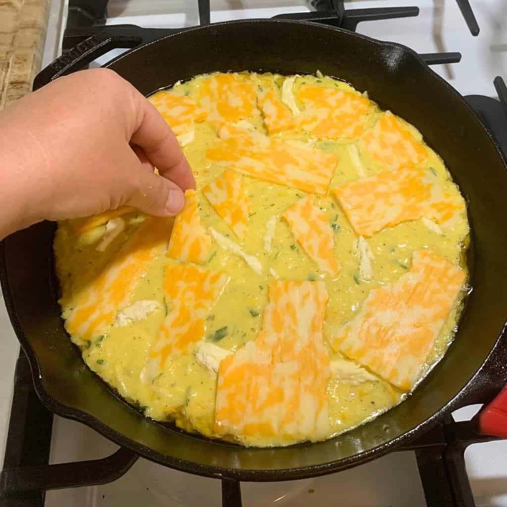 Woman topping zucchini casserole with cheese.