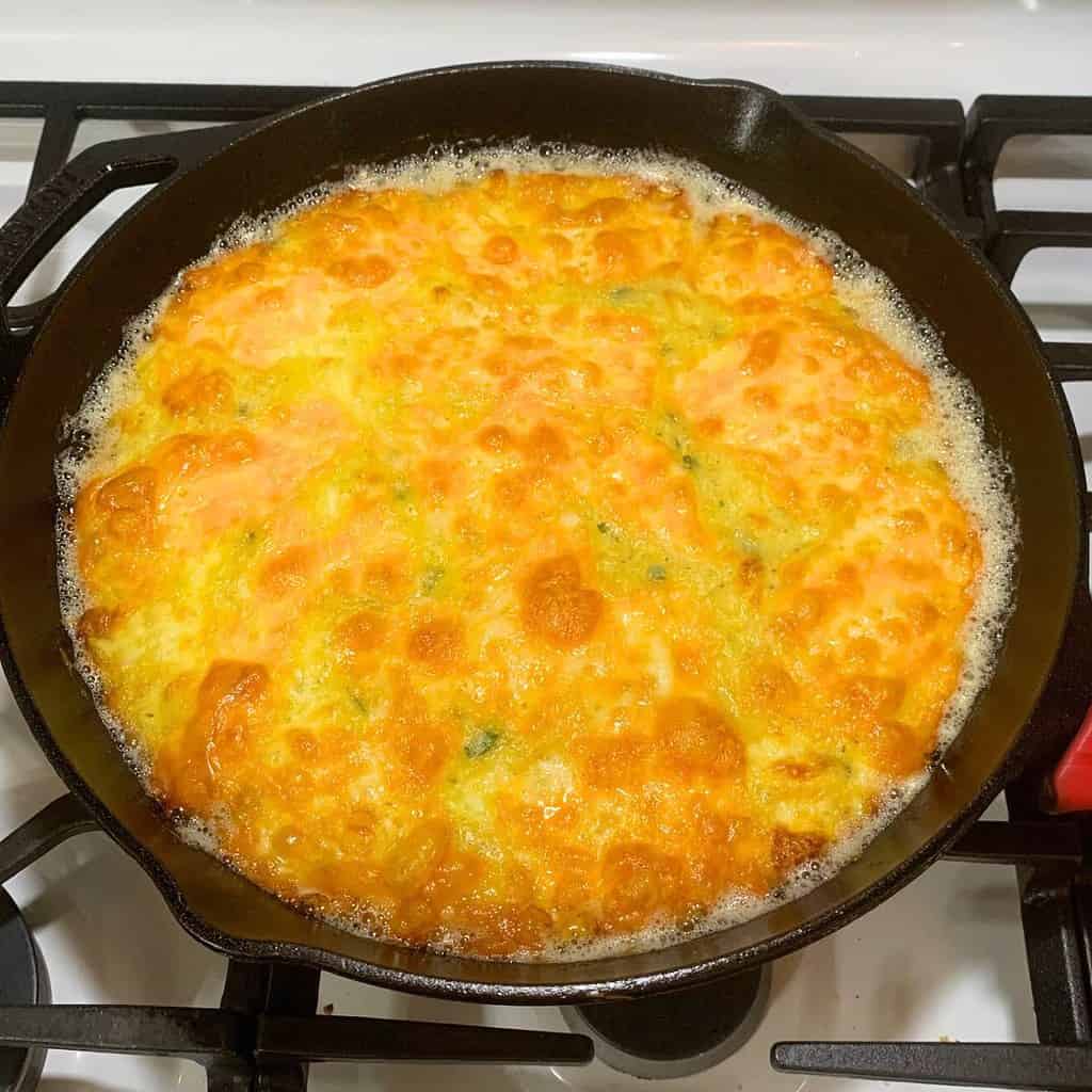 Freshly baked cheesy zucchini casserole in a cast iron skillet on the stove.