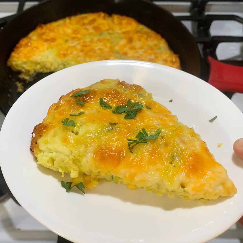 Woman holding a white plate with cheesy zucchini casserole that's fresh from the oven. A sprinkle of fresh parsley is on top.