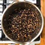 Dried elderberries, echinacea, and astragalus root covered with water in a stainless steel pot on the stove.