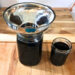 Two glass mason jars of elderberry syrup sitting on a wooden cutting board.