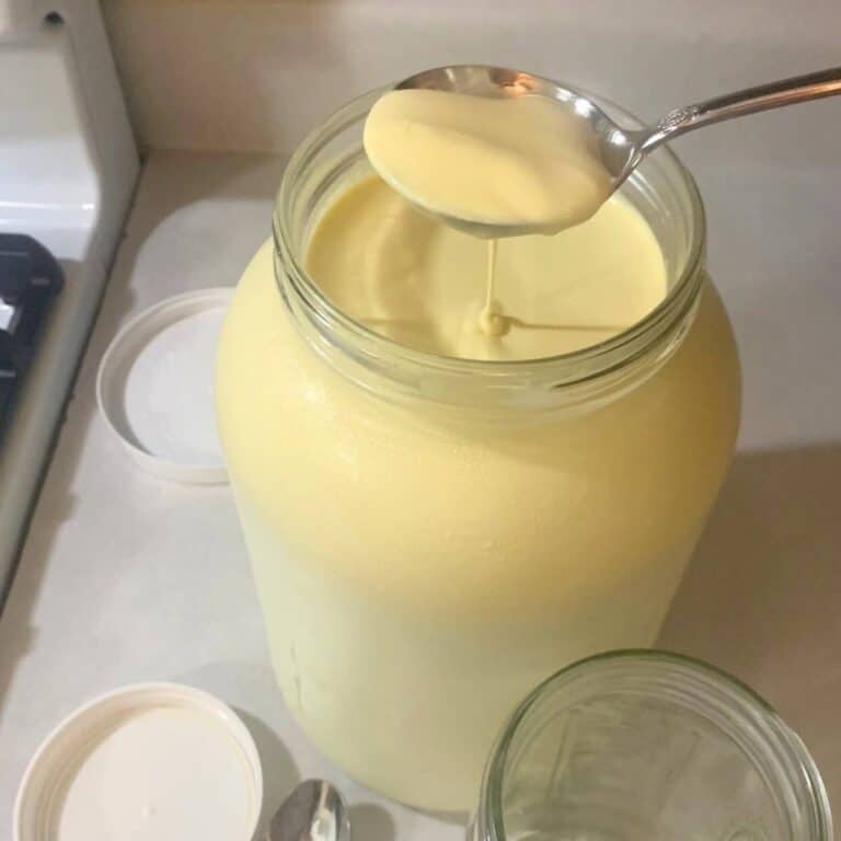 Woman scooping heavy cream from a gallon glass jar of raw milk.