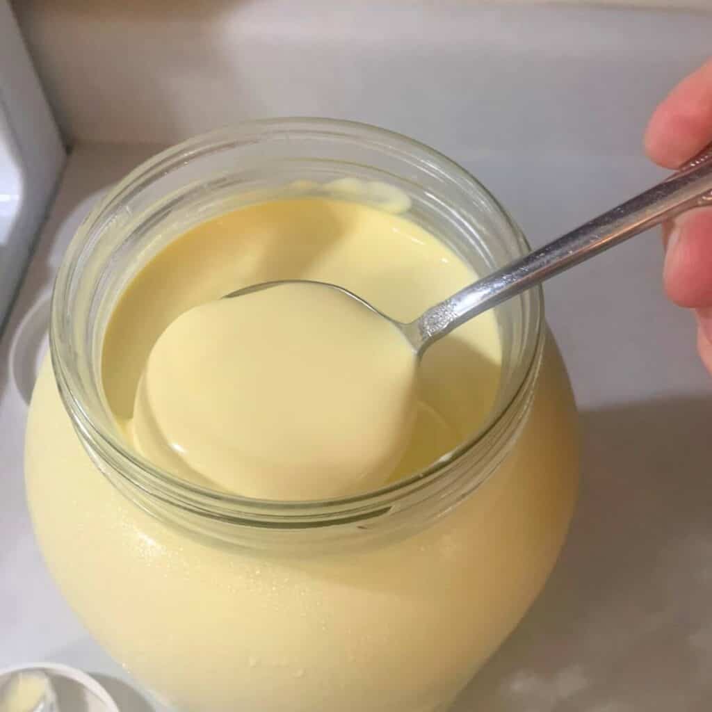 Woman scooping cream out of a glass mason jar of raw milk using a silver ladle.