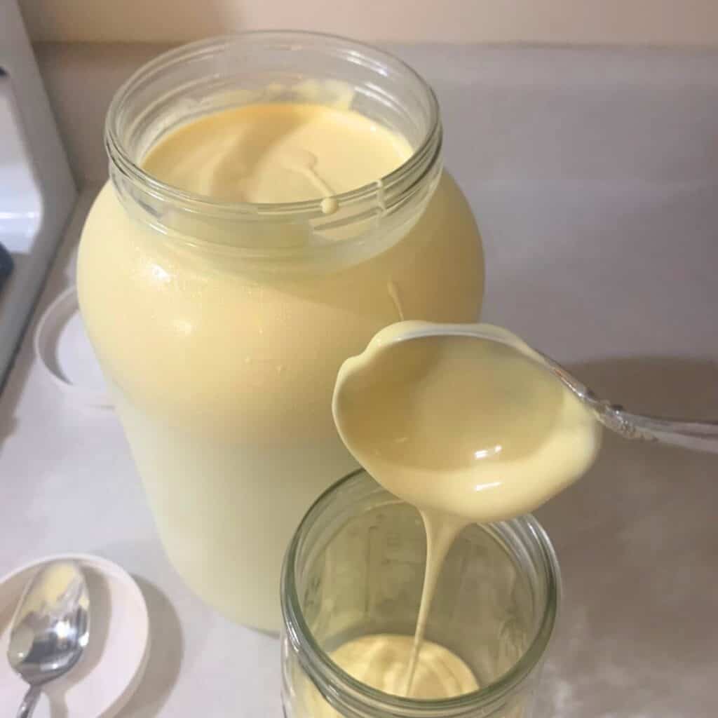 Woman pouring cream from a ladle into a glass mason jar.