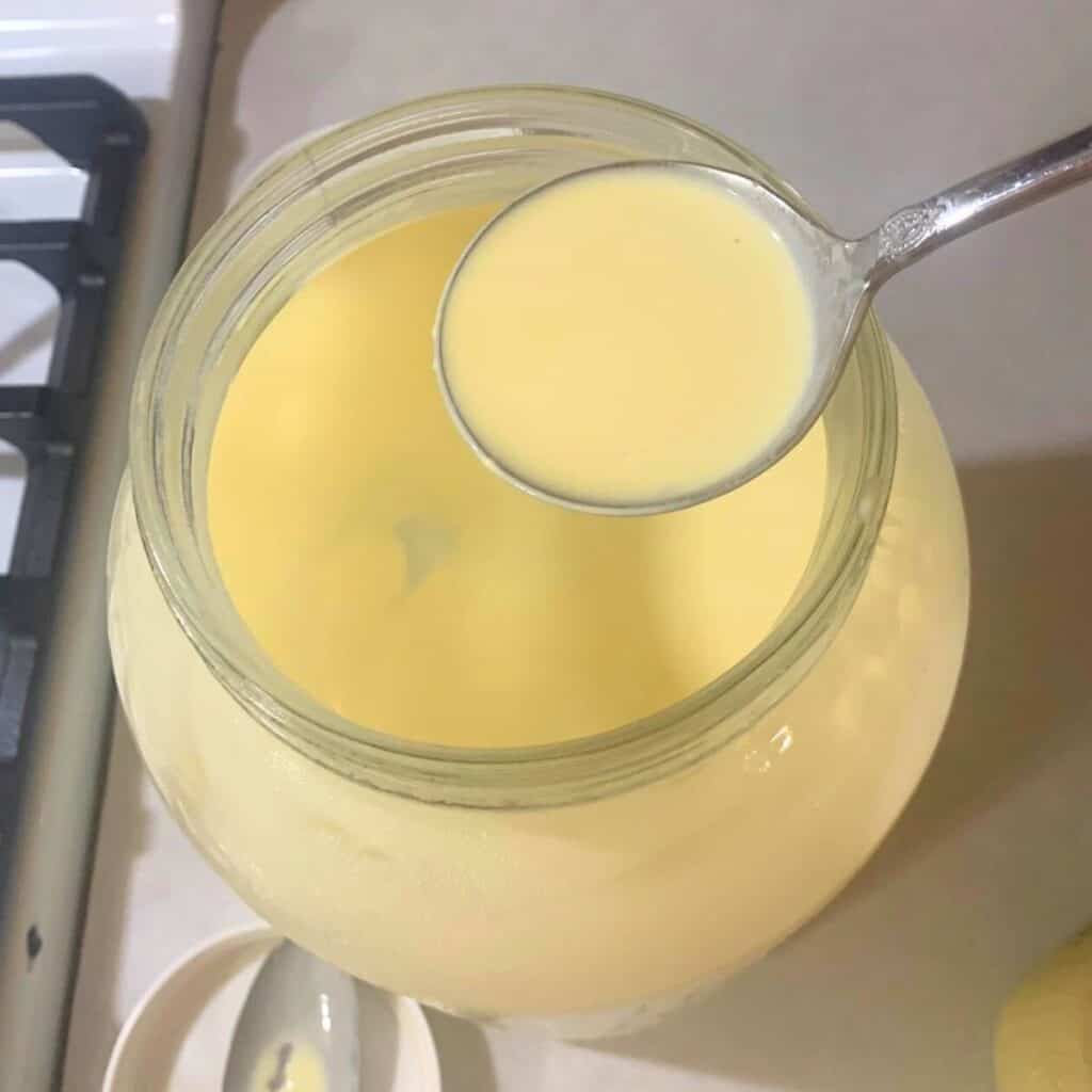 Woman skimming cream from raw milk in a glass mason jar using a silver ladle. 