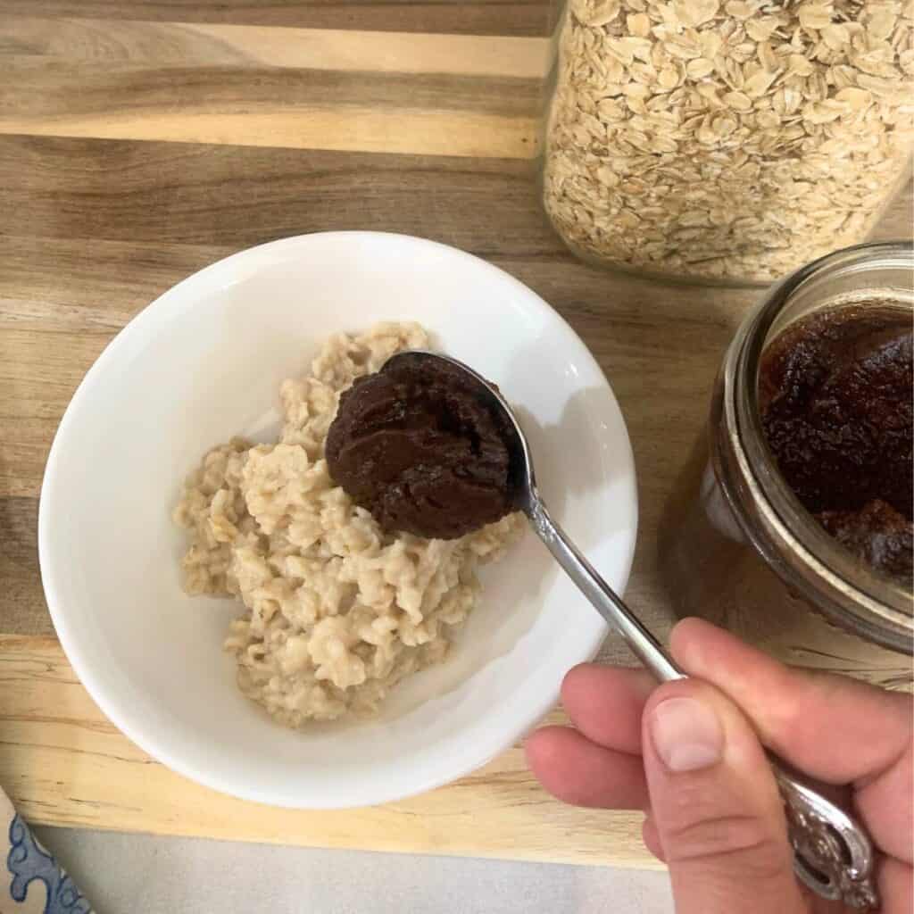 Woman mixing apple butter into a white bowl of cooked oatmeal.