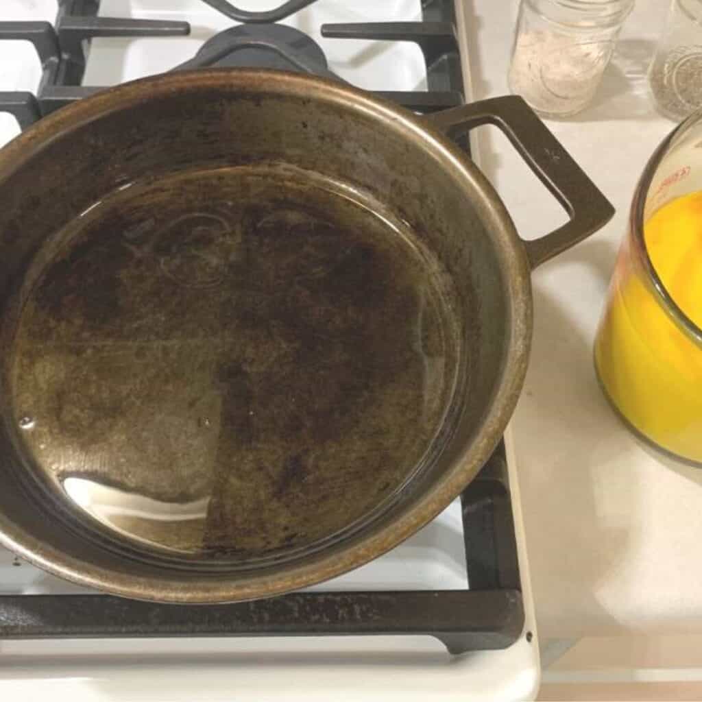 A cast iron skillet on a gas stove with melted bacon grease inside.