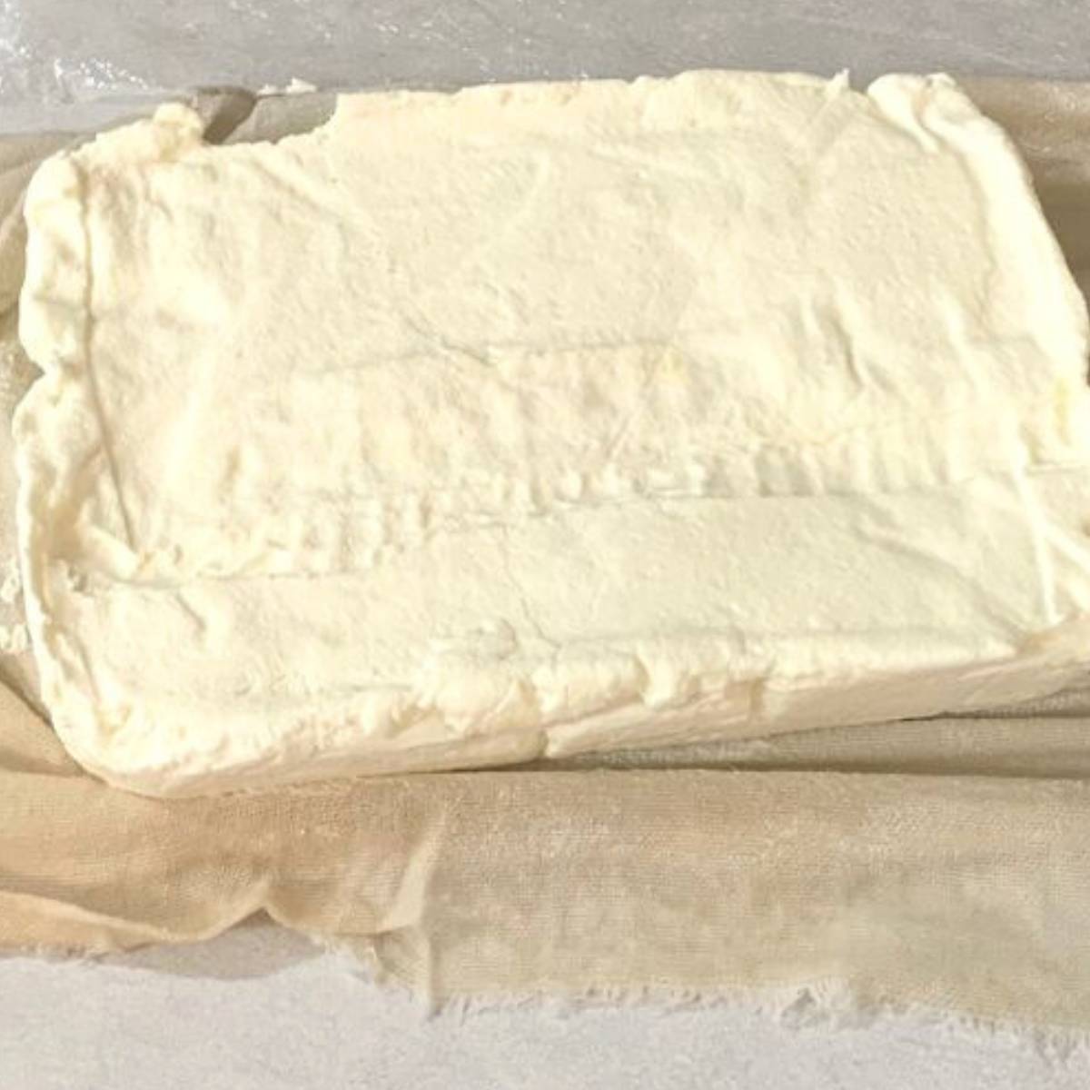 A block of homemade cream cheese sitting on a white flour sack towel.