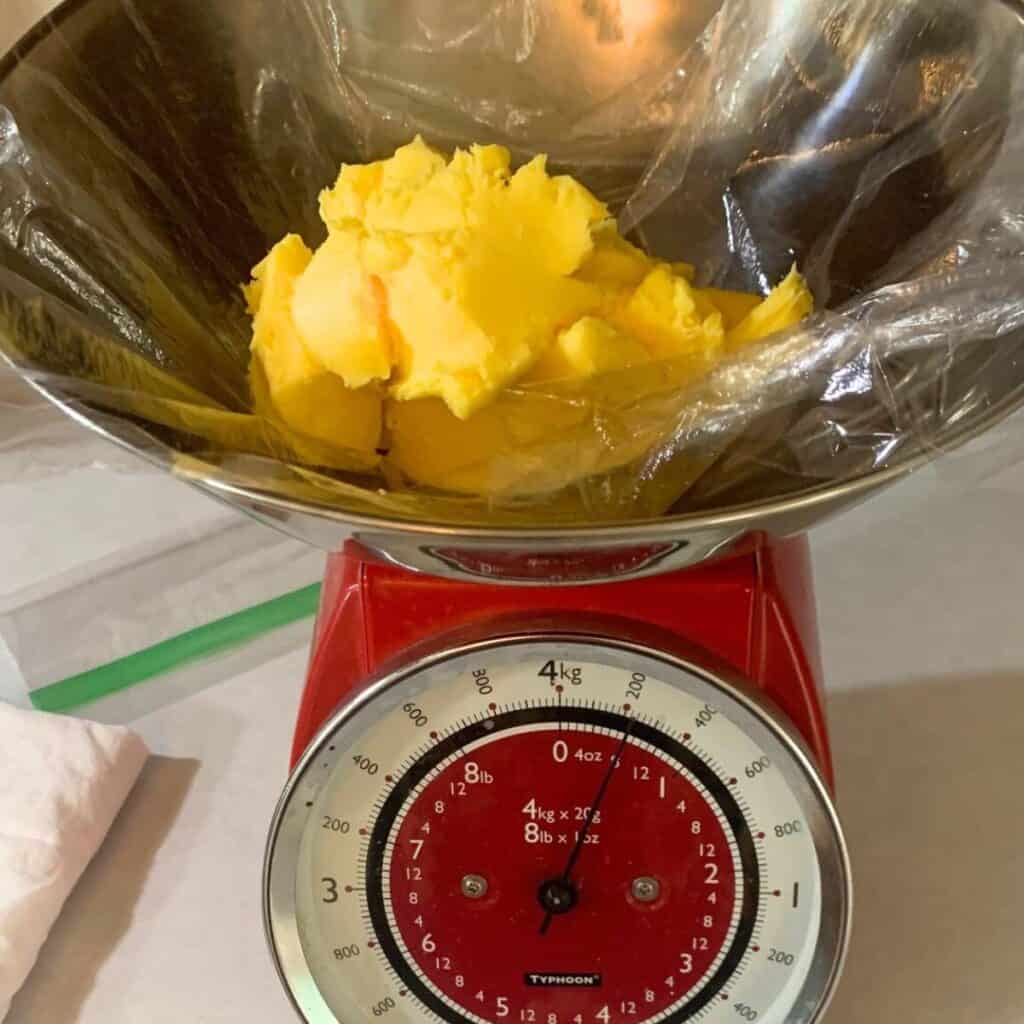 Homemade butter in plastic wrap sitting on a mechanical kitchen scale.