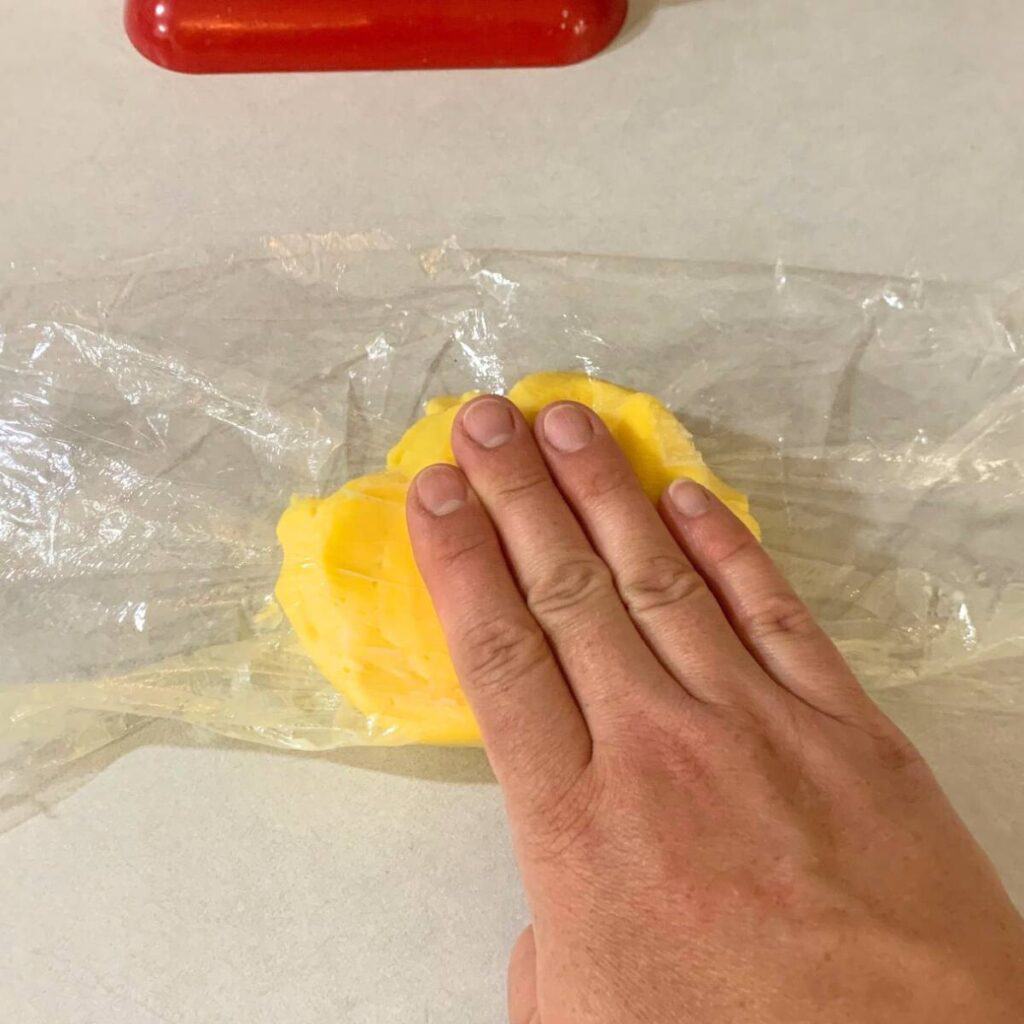 Woman pressing butter wrapped in plastic wrap.