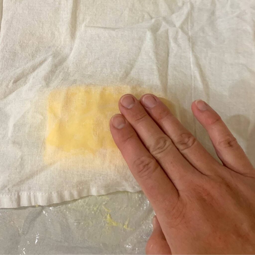 Woman pressing homemade butter with white flour sack towel that is soaking up excess buttermilk.