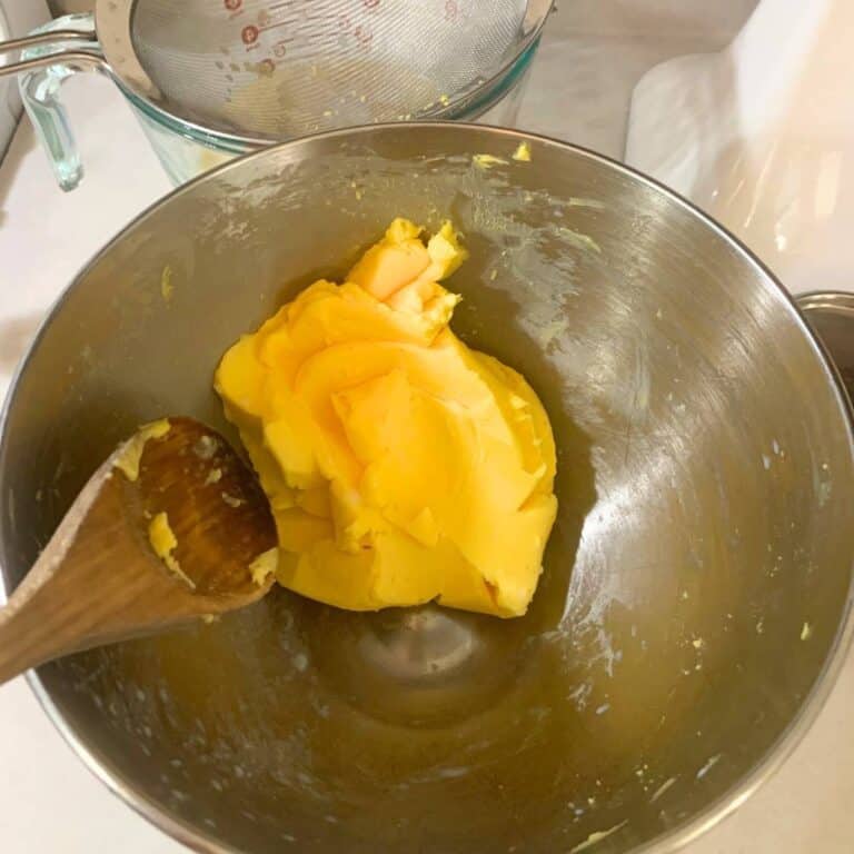 Woman pressing homemade butter against the side of a stainless steel mixing bowl using a wooden spoon.