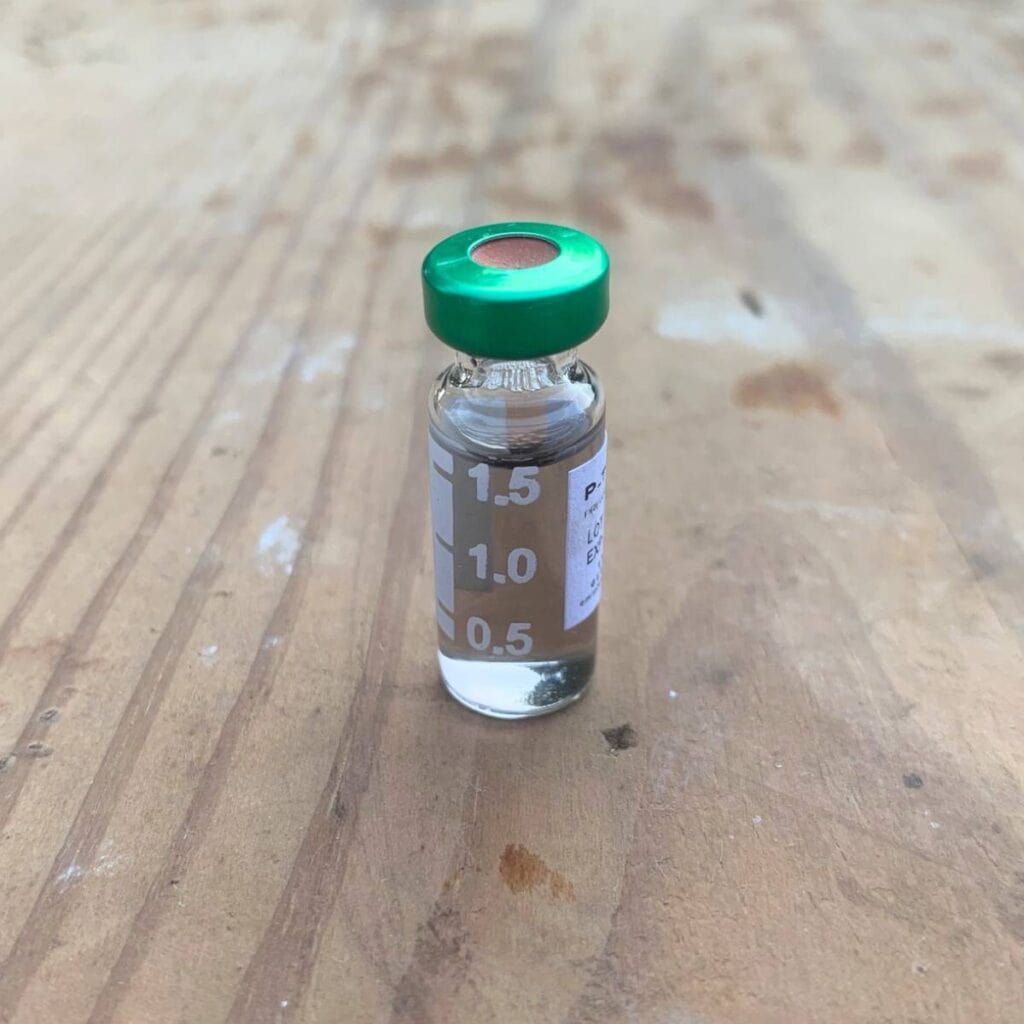 A glass vial with a green lid of clear urine sitting on a wood board.