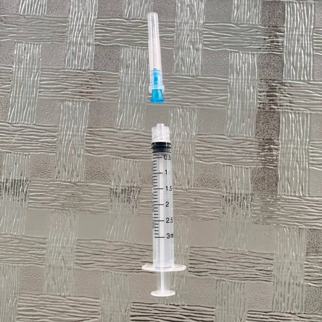 A plastic syringe with the needle off, sitting on a glass table.