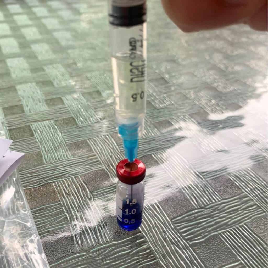 Woman inserting the needle of a plastic syringe into the red lid of a glass vial..