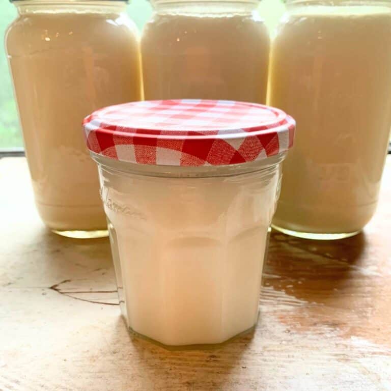 Four glass jars of homemade lard sitting on a scratched, white table.