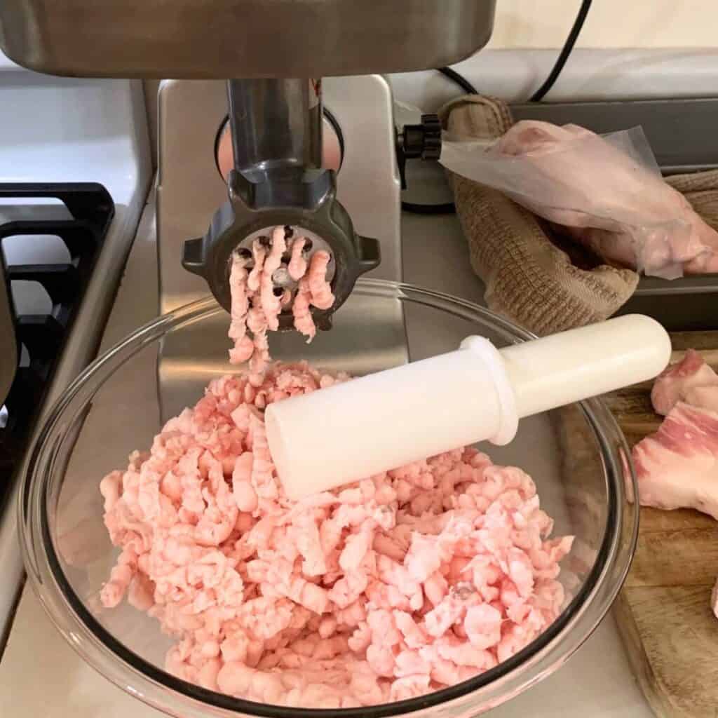 Pork fat going through a meat grinder and into a glass bowl.