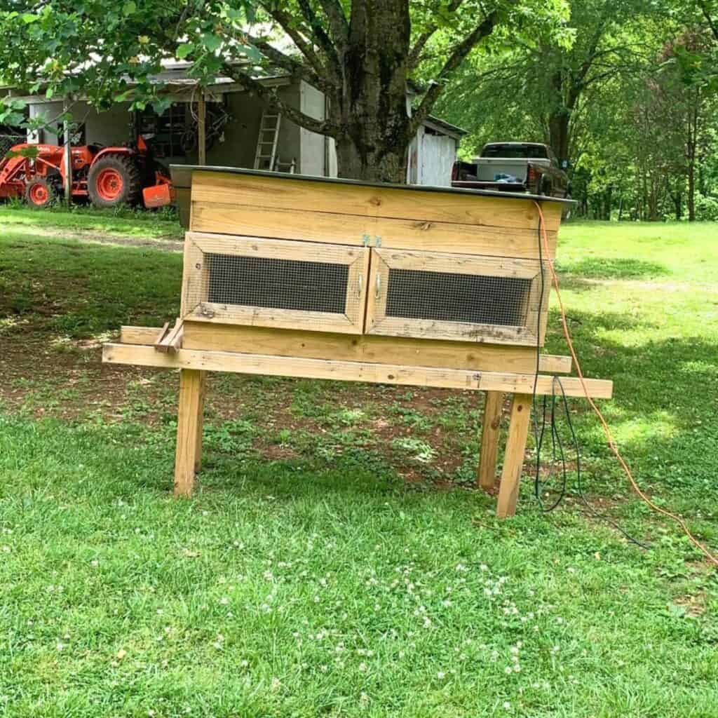 A wooden chicken brooder on green grass.