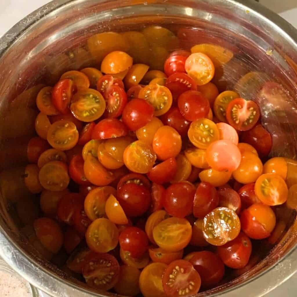 A silver bowl of red and orange cherry tomatoes that have been cut open down the middle.