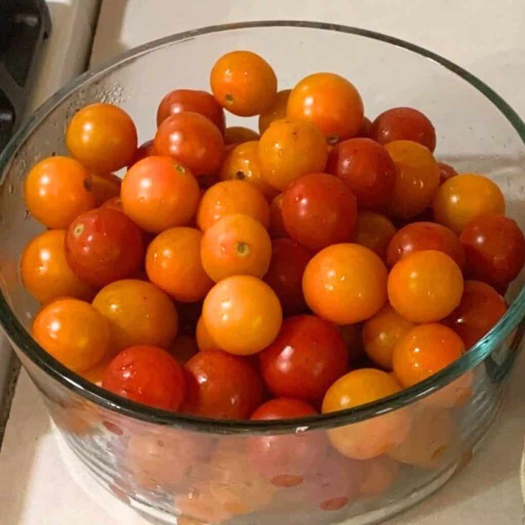 A glass bowl of fresh red and orange cherry tomatoes.