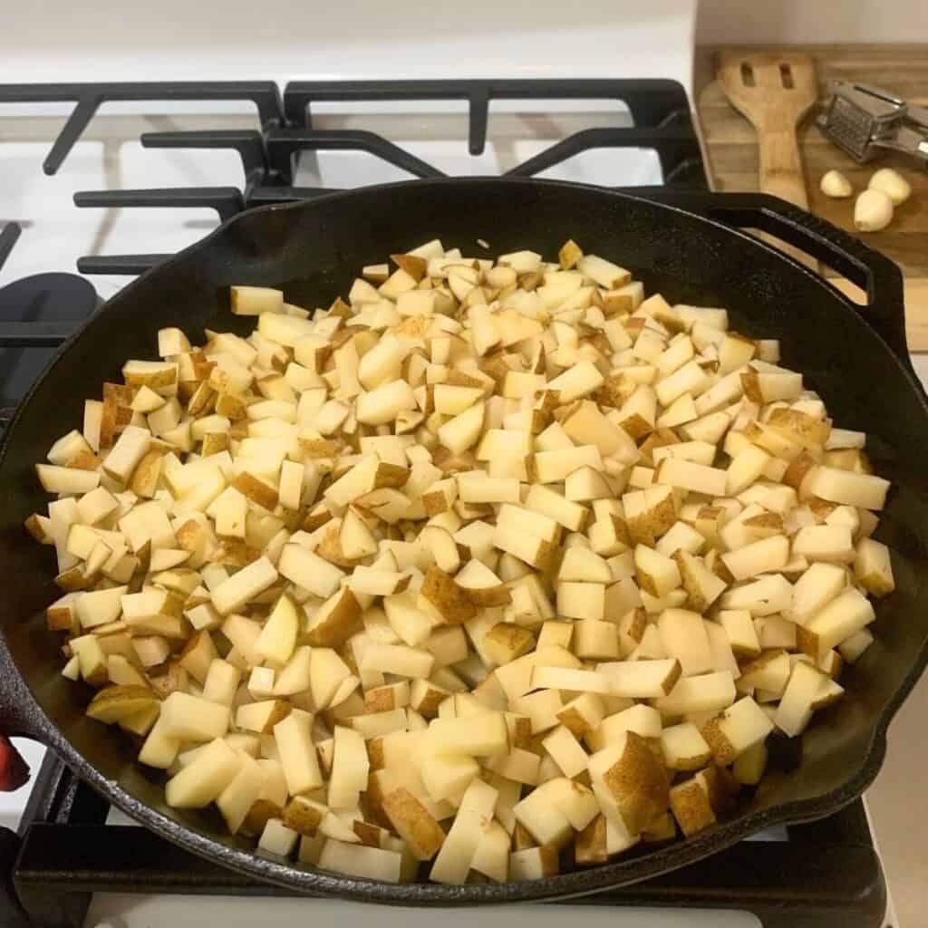 Diced potatoes inside a cast iron skillet on the stove.