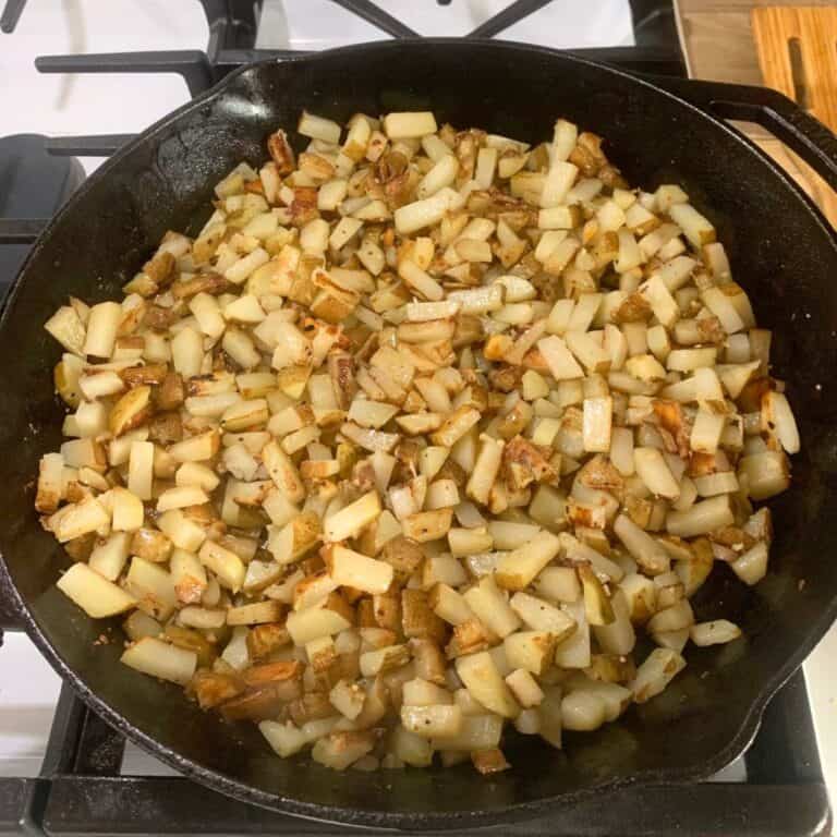 Seasoned, fried potatoes in a cast iron skillet on the stove.