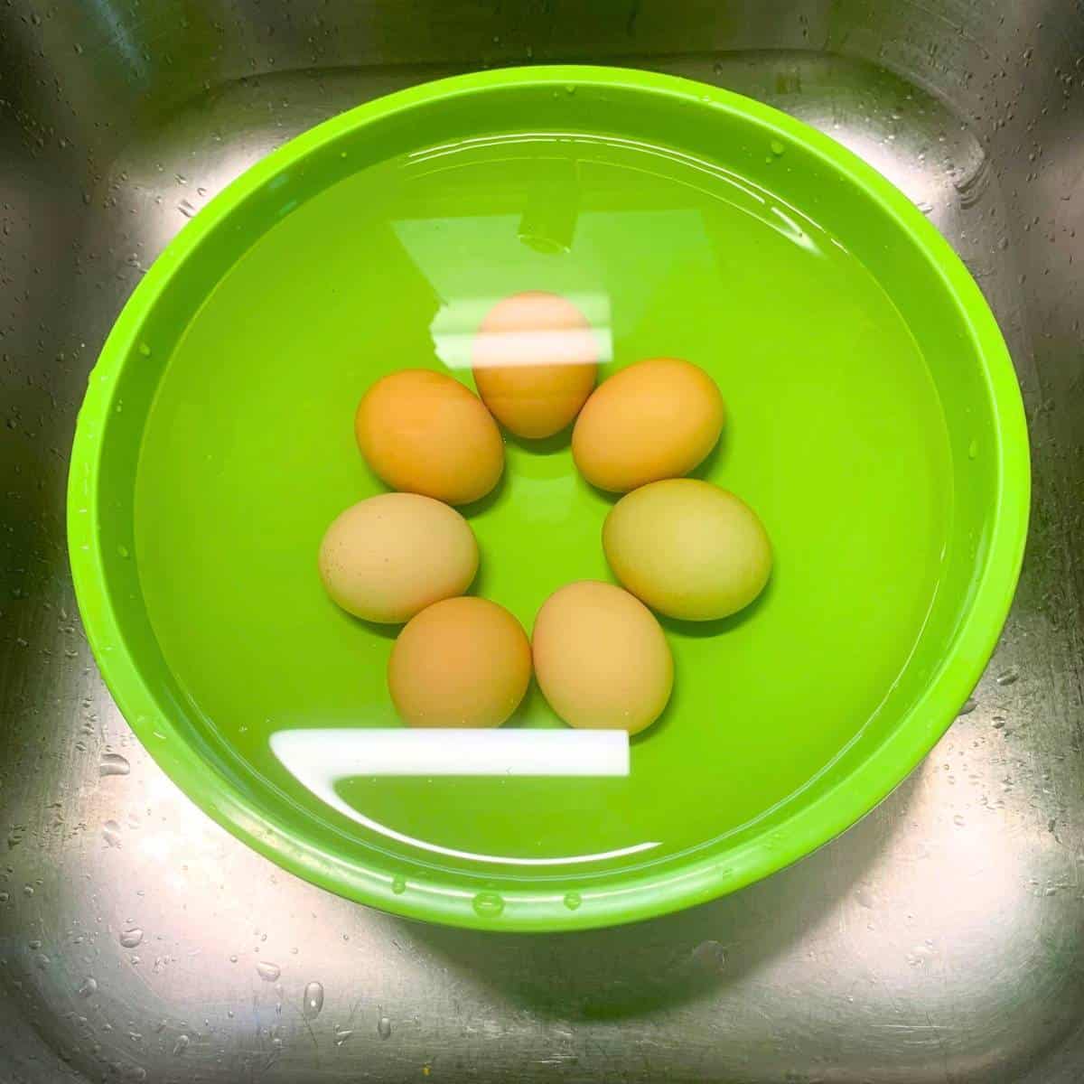 Eggs in a green bowl filled with water. The eggs sank to the bottom of the bowl.