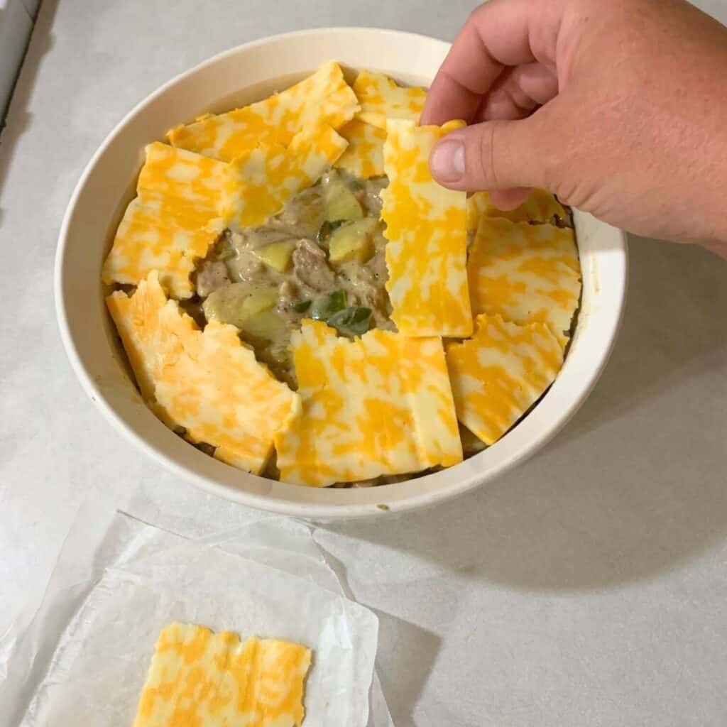 Woman putting cheese on top of ham and potato mixture in a white casserole dish.