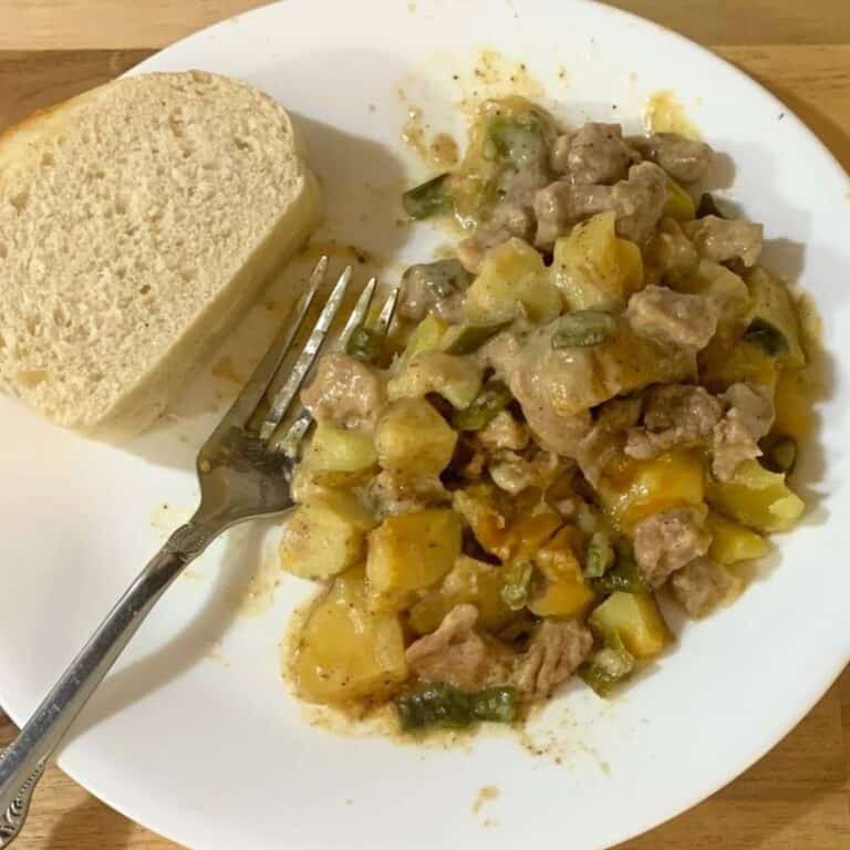 Ham, potato, and cheese casserole on a white plate with a slice of homemade french bread.