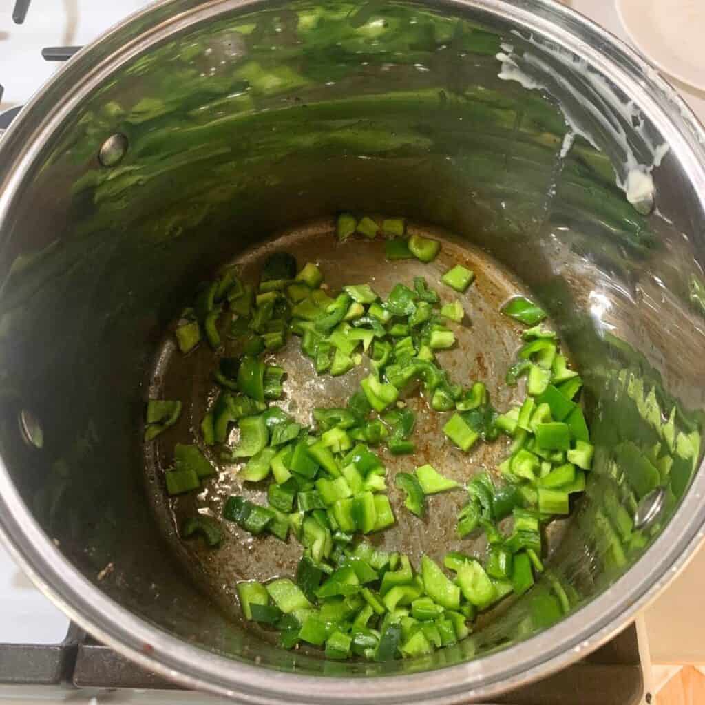 Diced green peppers cooking in a large stainless steel pot on a gas stove.