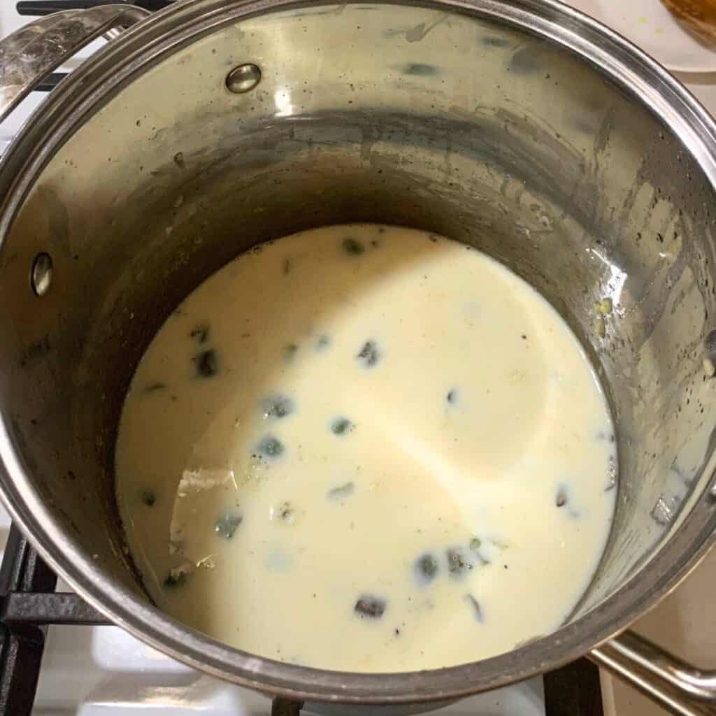 Stainless steel pot on a gas stove with cooked green peppers, flour, and milk.