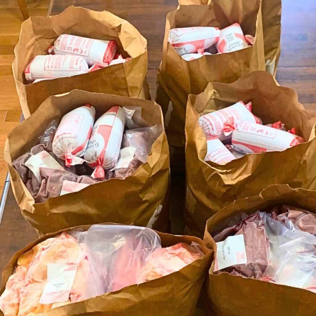 Six brown paper grocery bags filled with frozen beef cuts including ground beef, roasts, and steaks.
