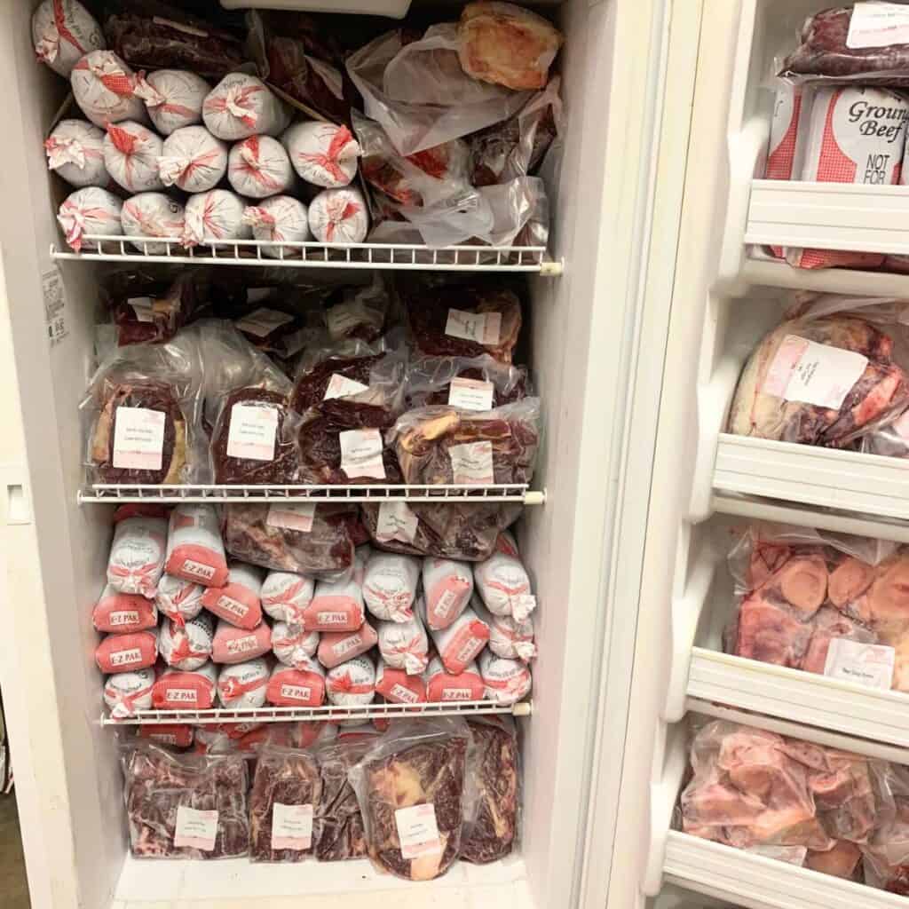 White upright freezer with the door open, showing it is filled with frozen cuts of beef on all four shelves plus the door shelves.