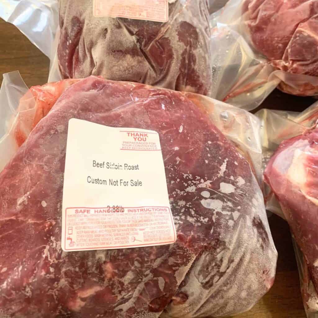 Several packages of frozen sirloin roast on a wooden kitchen table.