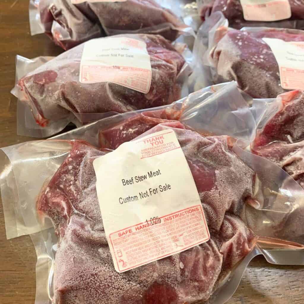 Several packages of frozen beef stew meat on a wooden kitchen table.