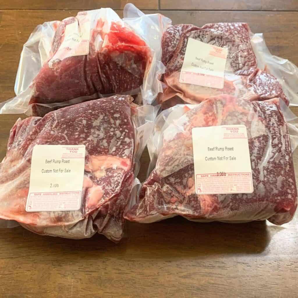 Four packages of frozen beef rump roasts on a wooden kitchen table.