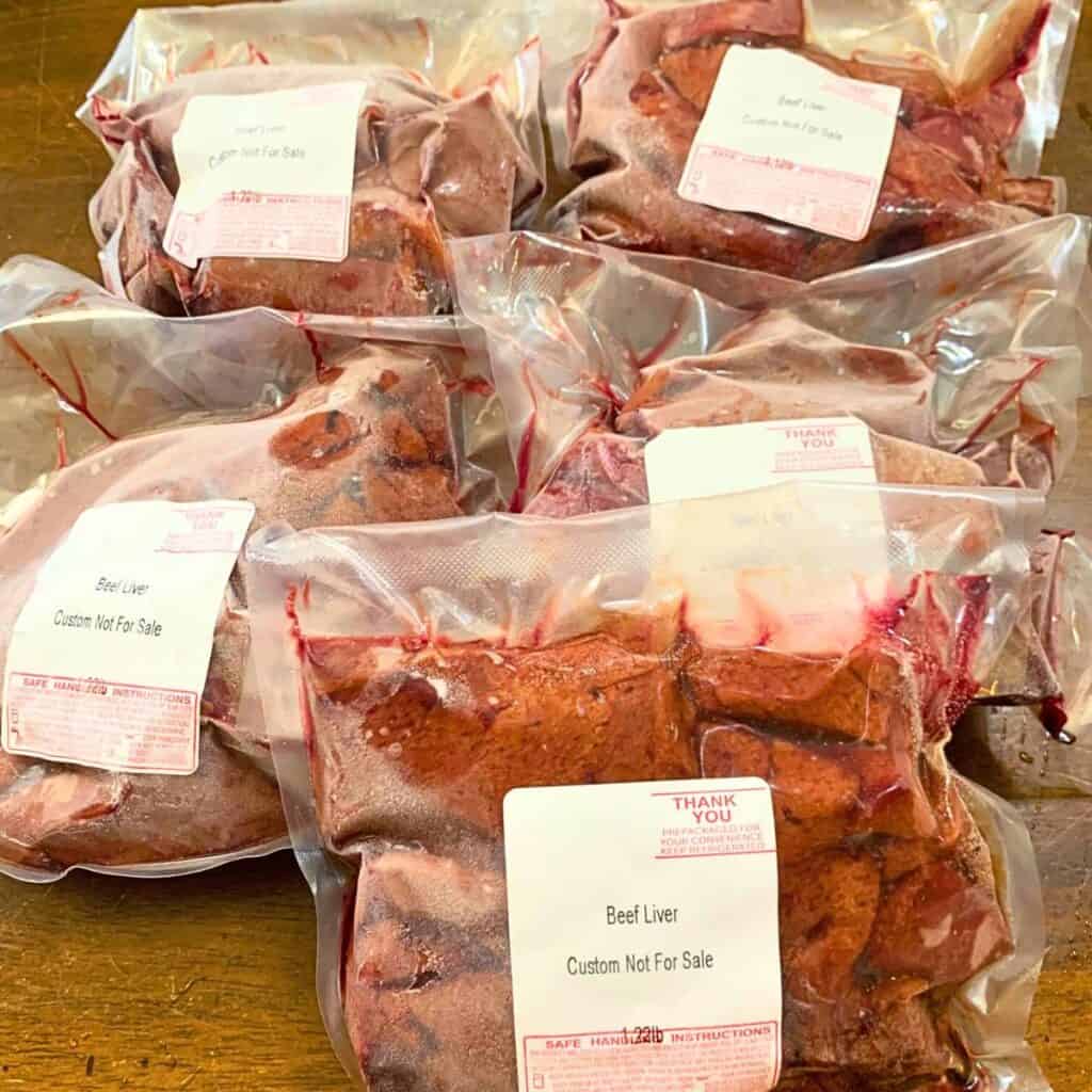 Individual packages of frozen beef livers on a wooden kitchen table.