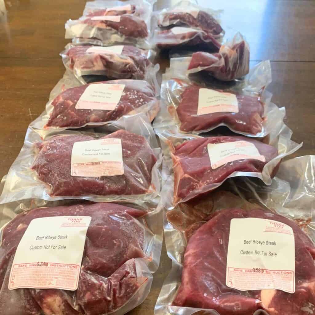 Several packages of frozen beef ribeye steaks on a wooden kitchen table.