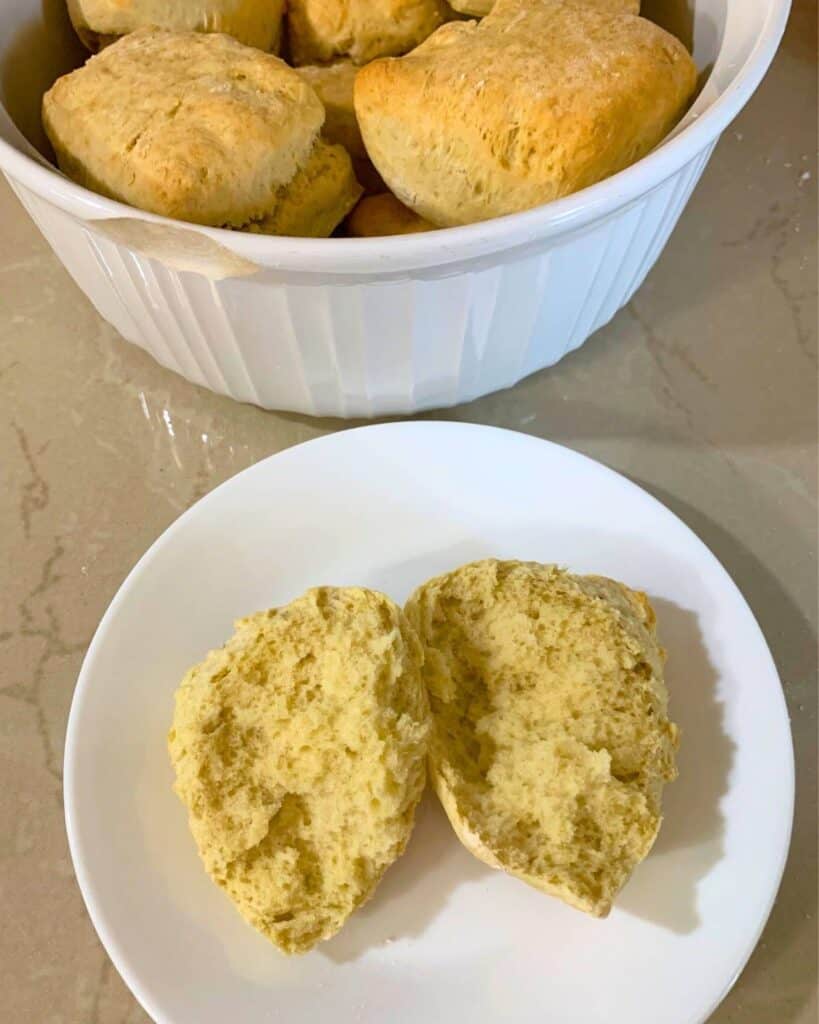 A white bowl of golden brown biscuits and a biscuit cut in half on a white plate.